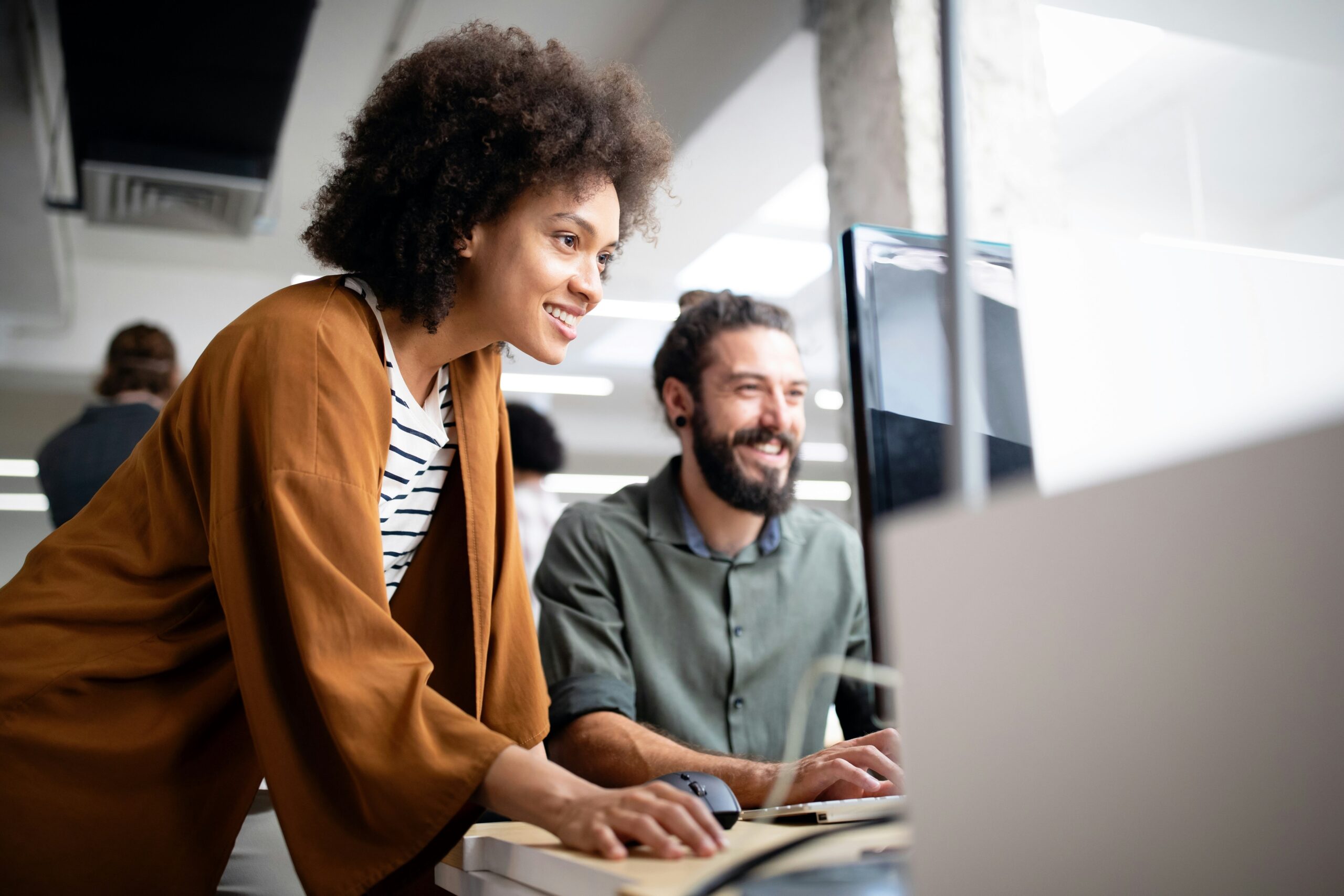 Two colleagues working together at a desktop computer in an office