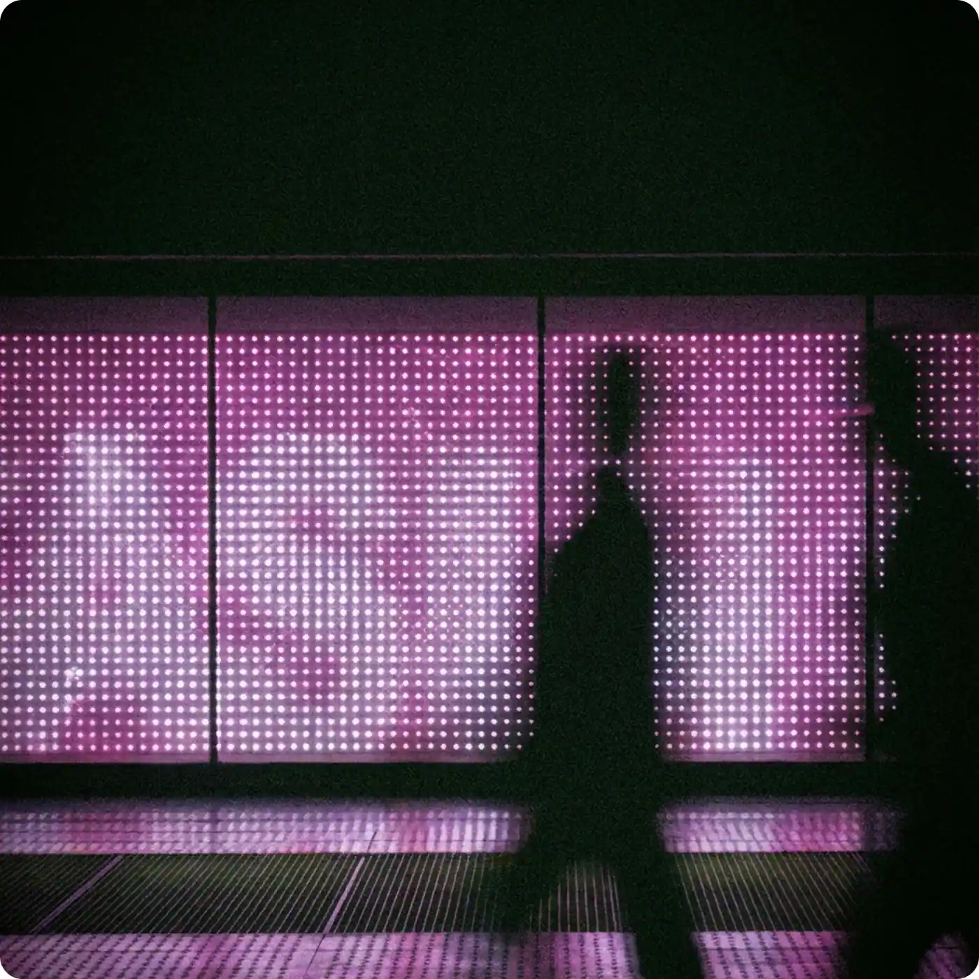 Silhouettes walking past a large illuminated digital screen